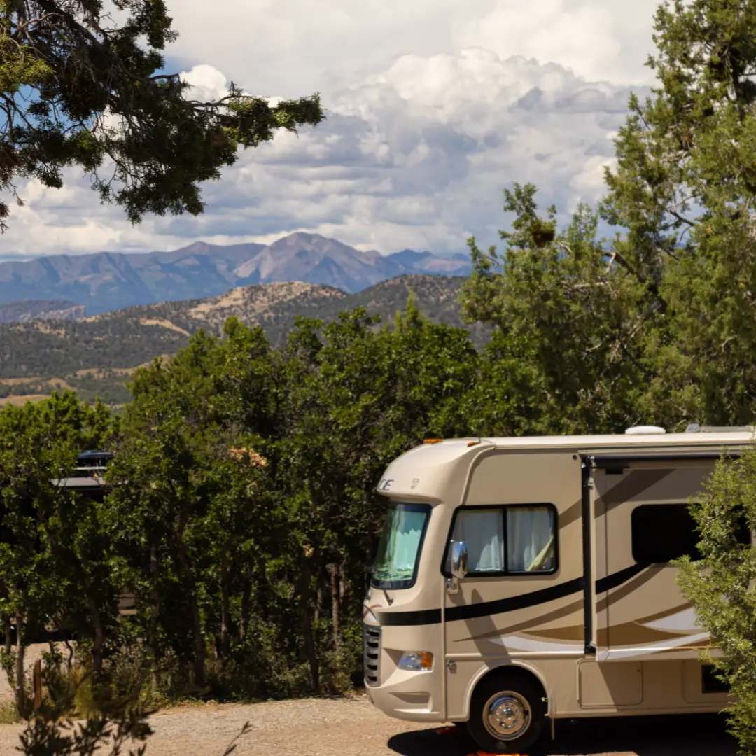 Amidst the towering trees, an RV is nestled against the stunning mountainous landscape of Durango, a perfect setting for spring adventures under a cloudy sky. .
