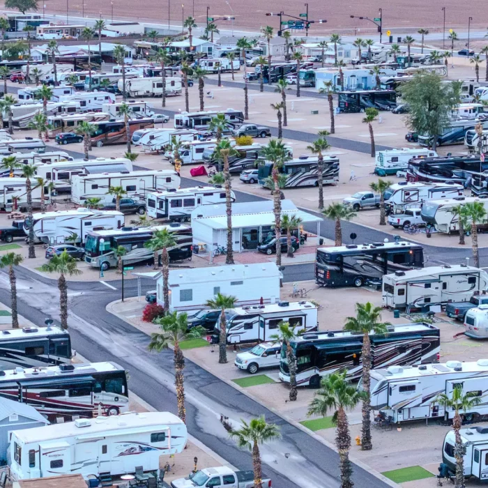 An aerial view of the Pueblo El Mirage RV park reveals numerous recreational vehicles nestled among rows of palm trees, offering a slice of winter bliss against the stunning Arizona desert backdrop.