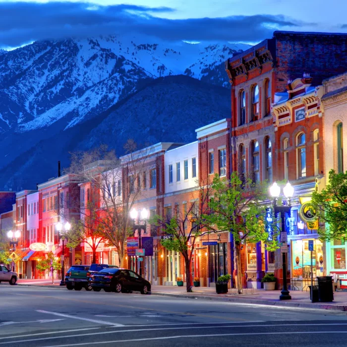 A vibrant, historic street with brick buildings at dusk, framed by snow-capped mountains in the background, invites travelers to enjoy an RV stay at Park City RV Resort—a perfect start to New Year 2025.