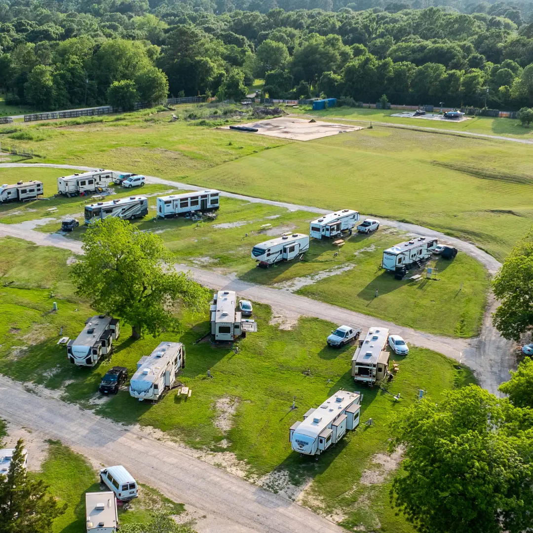An aerial view of a campground at the water's edge reveals several RVs parked on grassy areas, surrounded by trees and greenery, offering the ultimate relaxation experience.