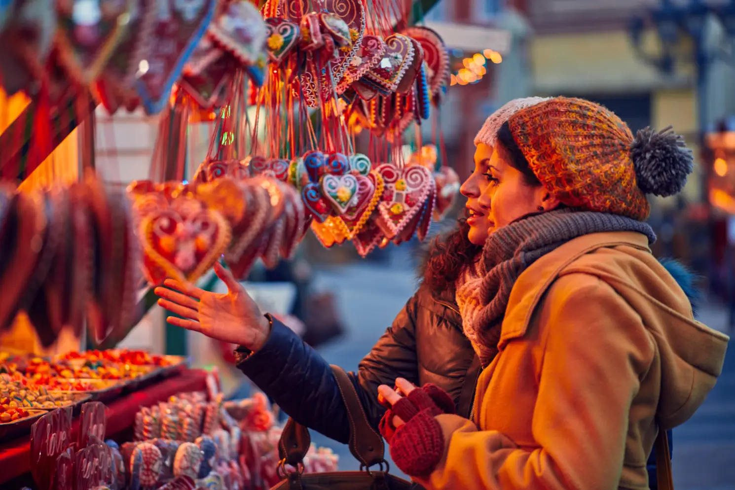 Two people in warm clothing enjoy a Thanksgiving getaway at Rayford Crossing, examining heart-shaped gingerbread cookies at an outdoor market stall.