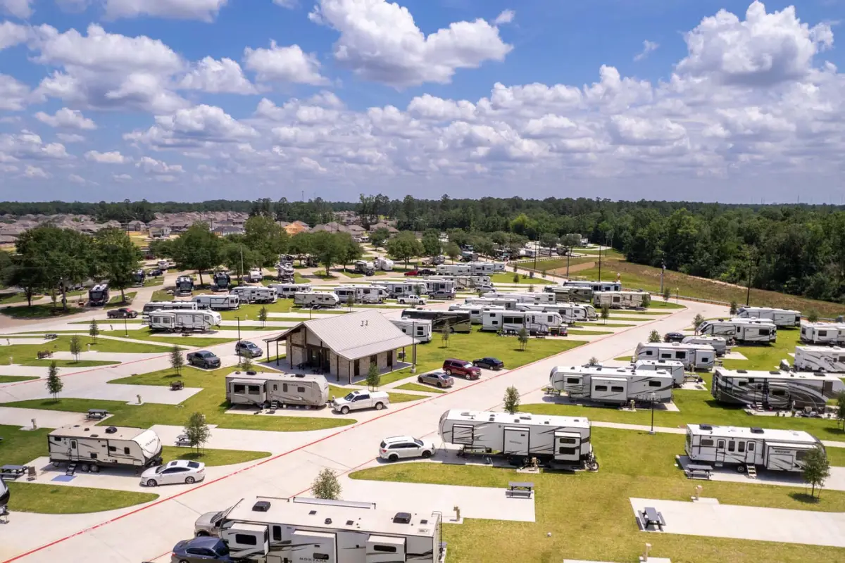 An aerial view of Rayford Crossing reveals an RV resort with numerous RVs parked on grassy lots surrounding a central building, all under a partly cloudy sky, perfect for memorable holidays.