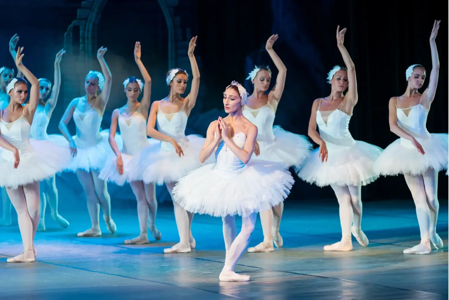 Ballet dancers in white tutus gracefully perform on stage, akin to a festive holiday scene, led by a central dancer basking in the spotlight.