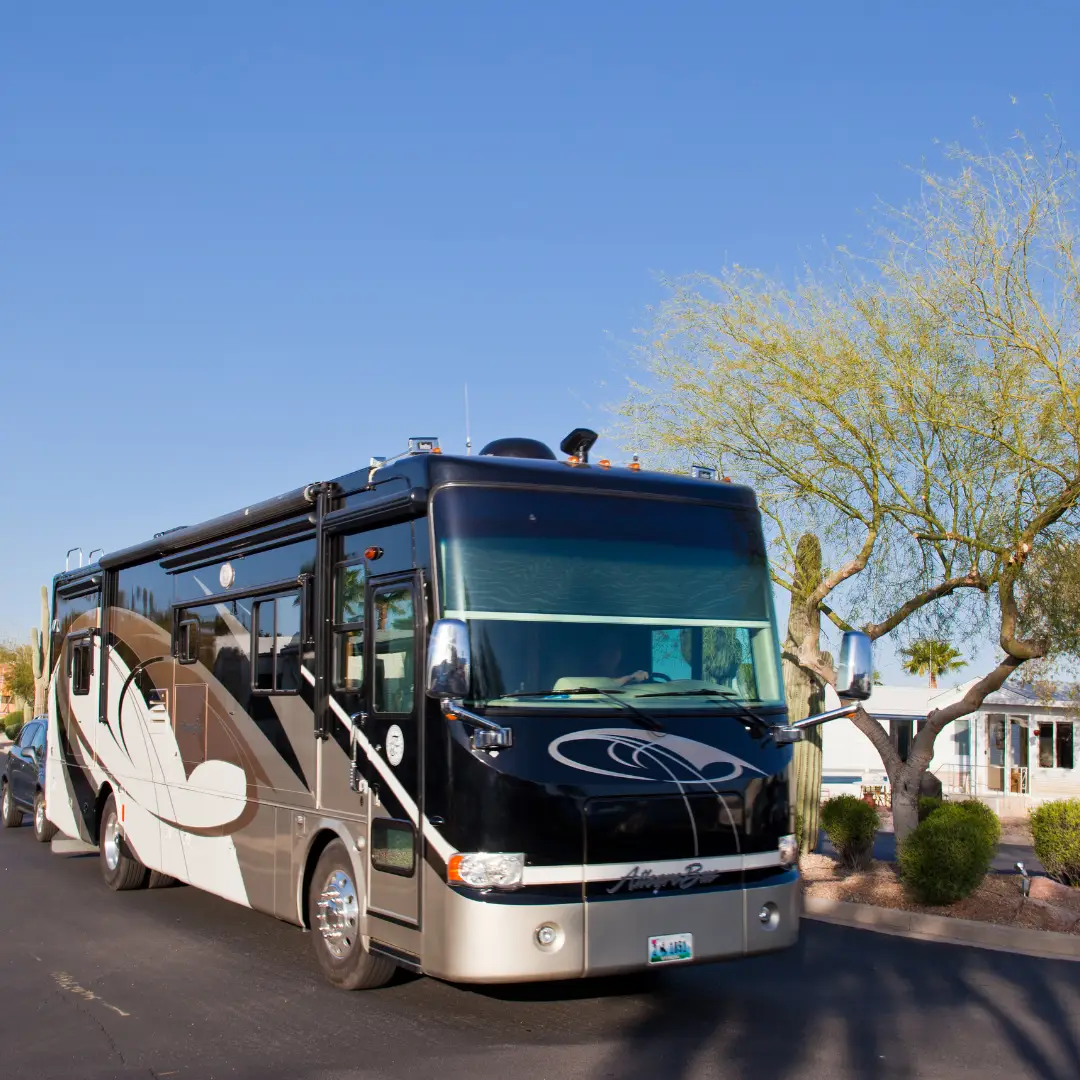 A large black and white RV parked on a suburban street, reminiscent of a stay at an RV resort in Gold Canyon, with trees and houses in the background under a clear blue sky.