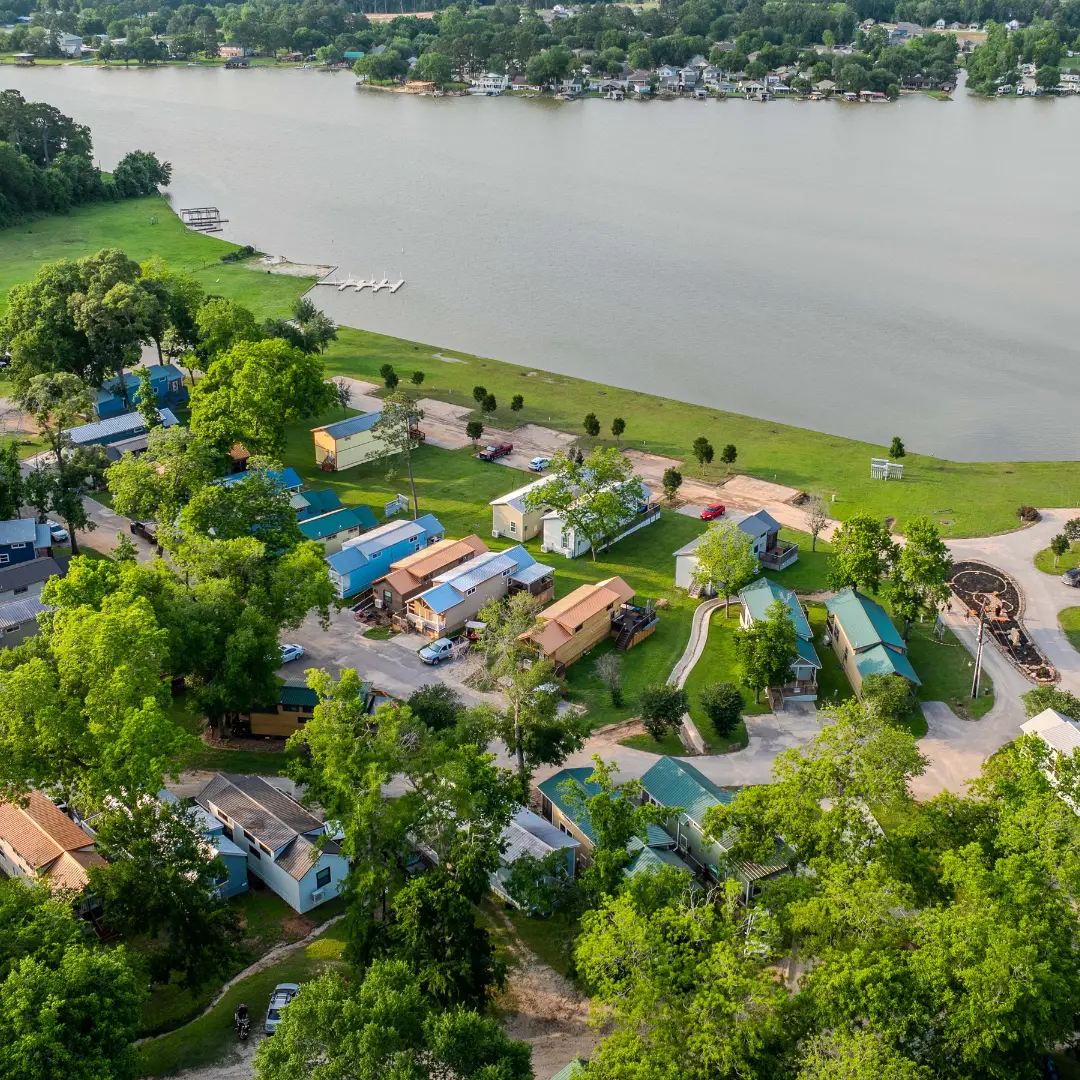 An aerial view of the Water's Edge neighborhood reveals charming houses nestled among green trees, with a serene river flowing in the background.