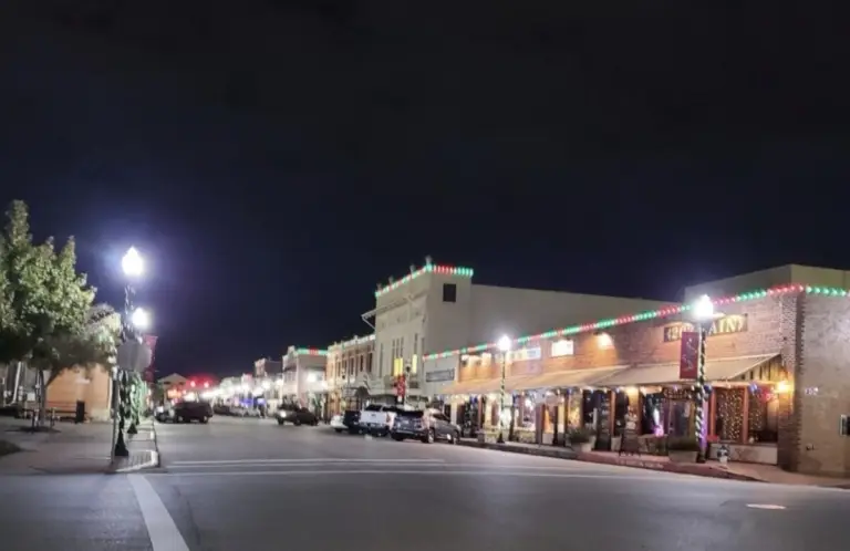 A quiet street at night near Rayford Crossing, with buildings adorned in festive lights, parked cars lining the road, and illuminated street lamps.