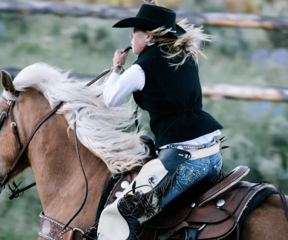A person wearing a cowboy hat and riding attire rides a brown horse with a flowing mane, captured in motion against a blurred background during their Durango summer adventure.