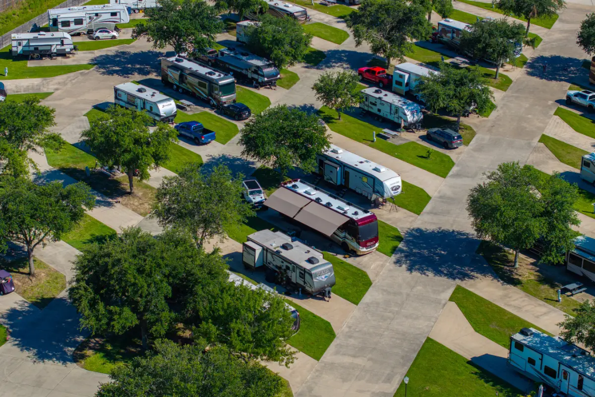 Aerial view of Rayford Crossing RV park, an ideal RV getaway with multiple recreational vehicles parked on paved lots, surrounded by green lawns and trees.