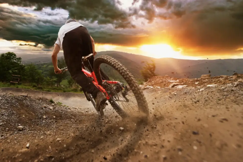 Person exploring Durango on a mountain bike, racing along a dirt trail during a dramatic sunset. Dust billows from the tires, capturing the essence of summer adventure ideas in this breathtaking scene.