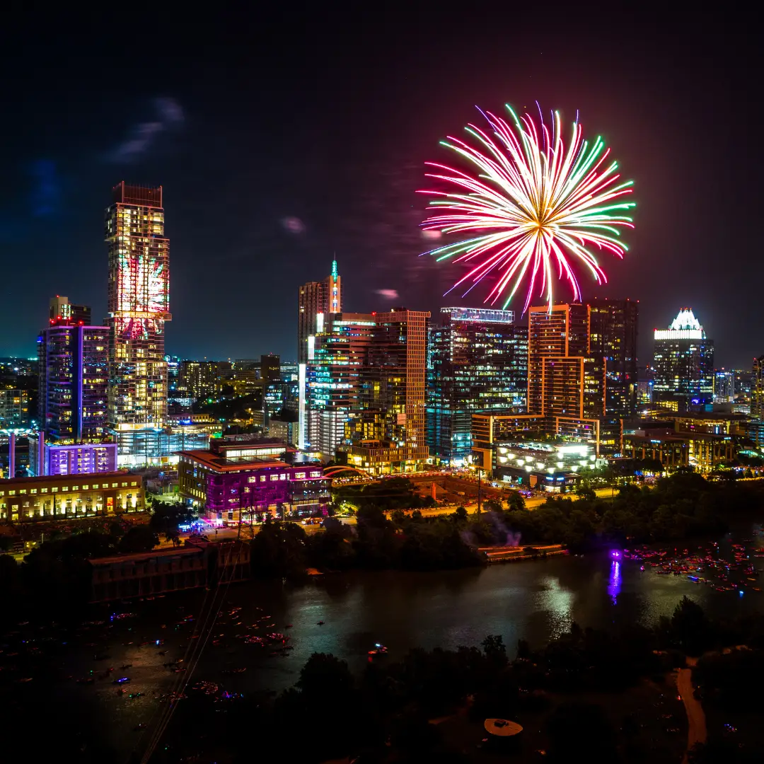 Fireworks burst over Austin's brightly lit city skyline at night, reflecting on the water below—a spectacular highlight of summer 2025 events.