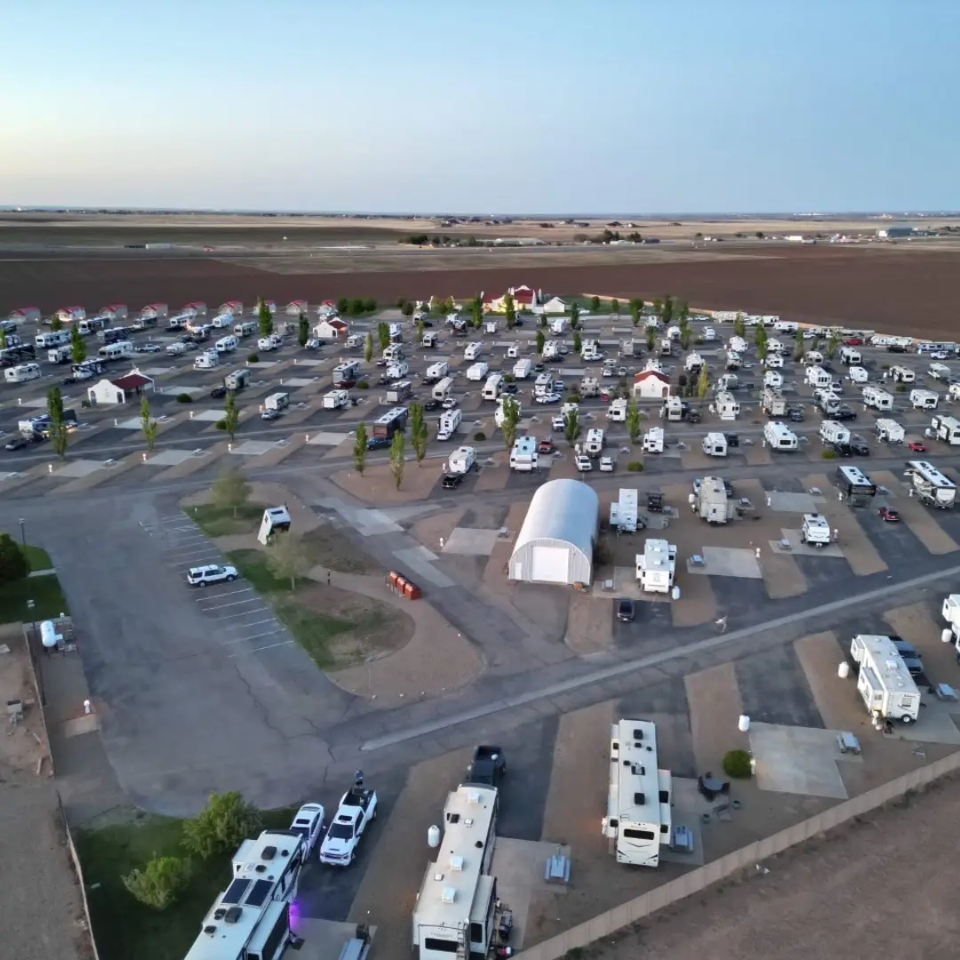 Aerial view of Oasis Amarillo RV park, a haven for long-term RV travelers. It features a grid layout with numerous RVs neatly parked in rows, surrounded by open fields and a sprinkling of trees.
