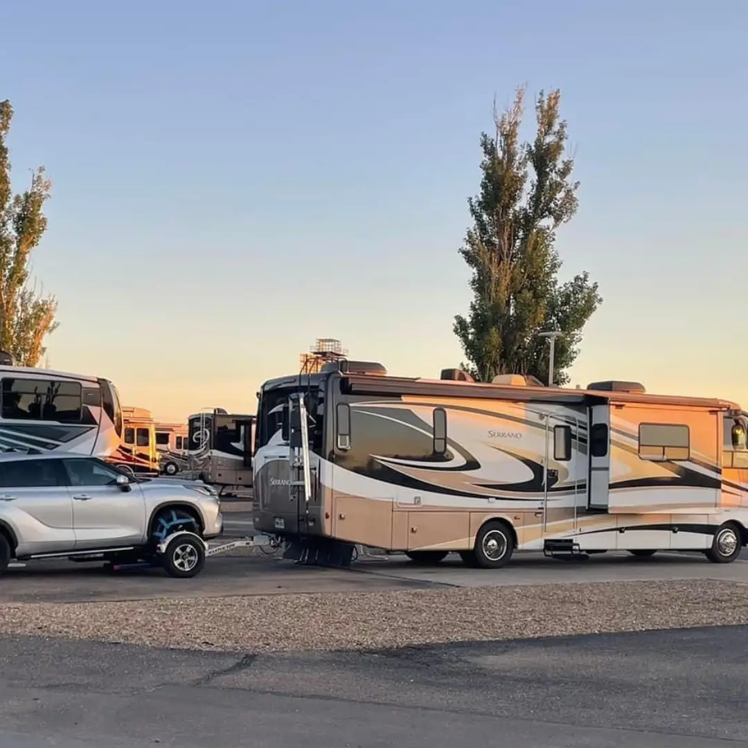 RVs parked in a campground at sunset serve as the ultimate RV overnight stop, with a vehicle hitched to one of them, offering weary travelers along the I-40 route a serene and restful retreat.