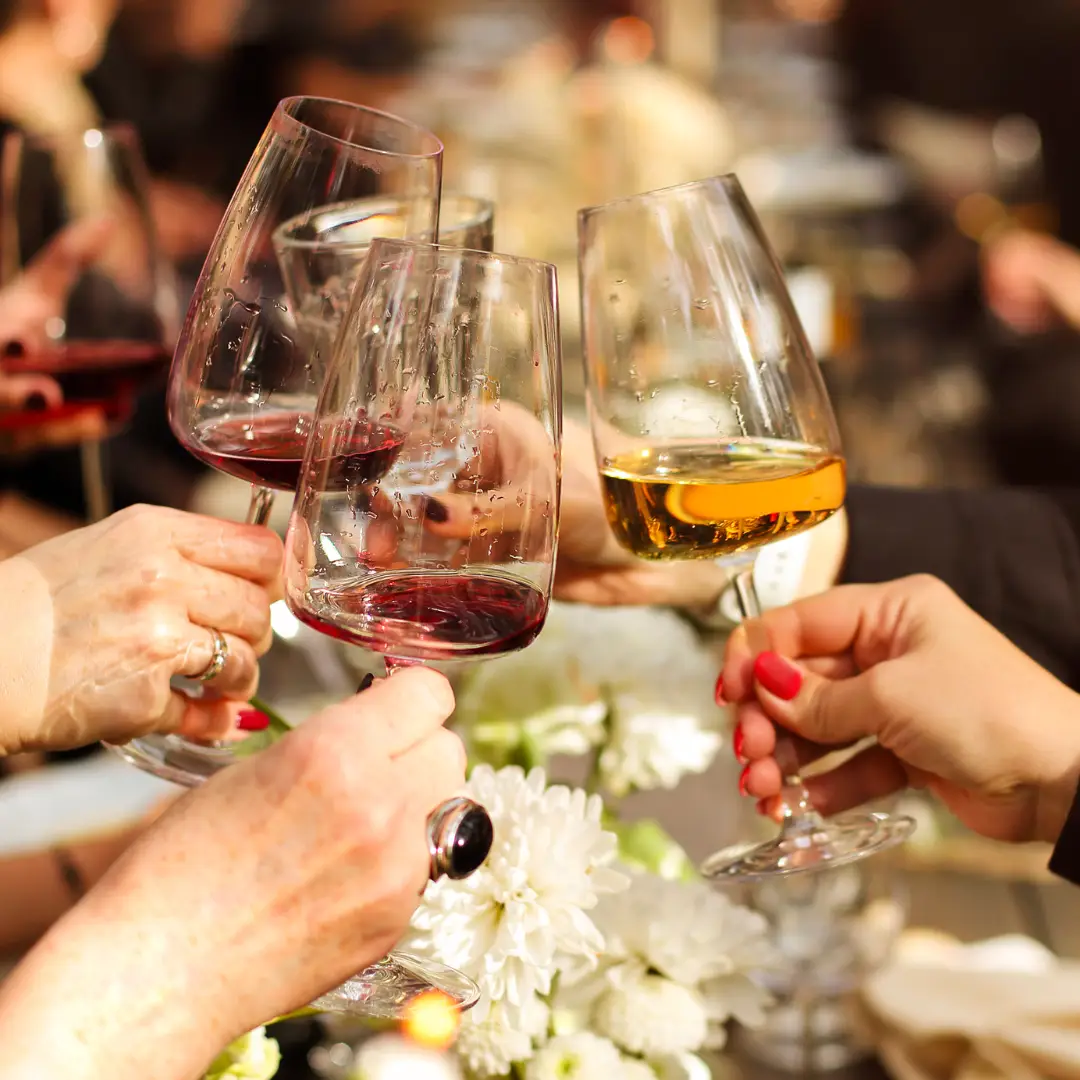A group of people clinking wine glasses together, celebrating a spring adventure at a gathering with a floral table centerpiece.