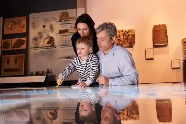 A family with a young child visits the museum, interacting with an exhibit reminiscent of the NASA Johnson Space Center. The child points excitedly at the display while the adults watch attentively, capturing a moment of wonder that feels just like exploring Houston’s own space marvels.