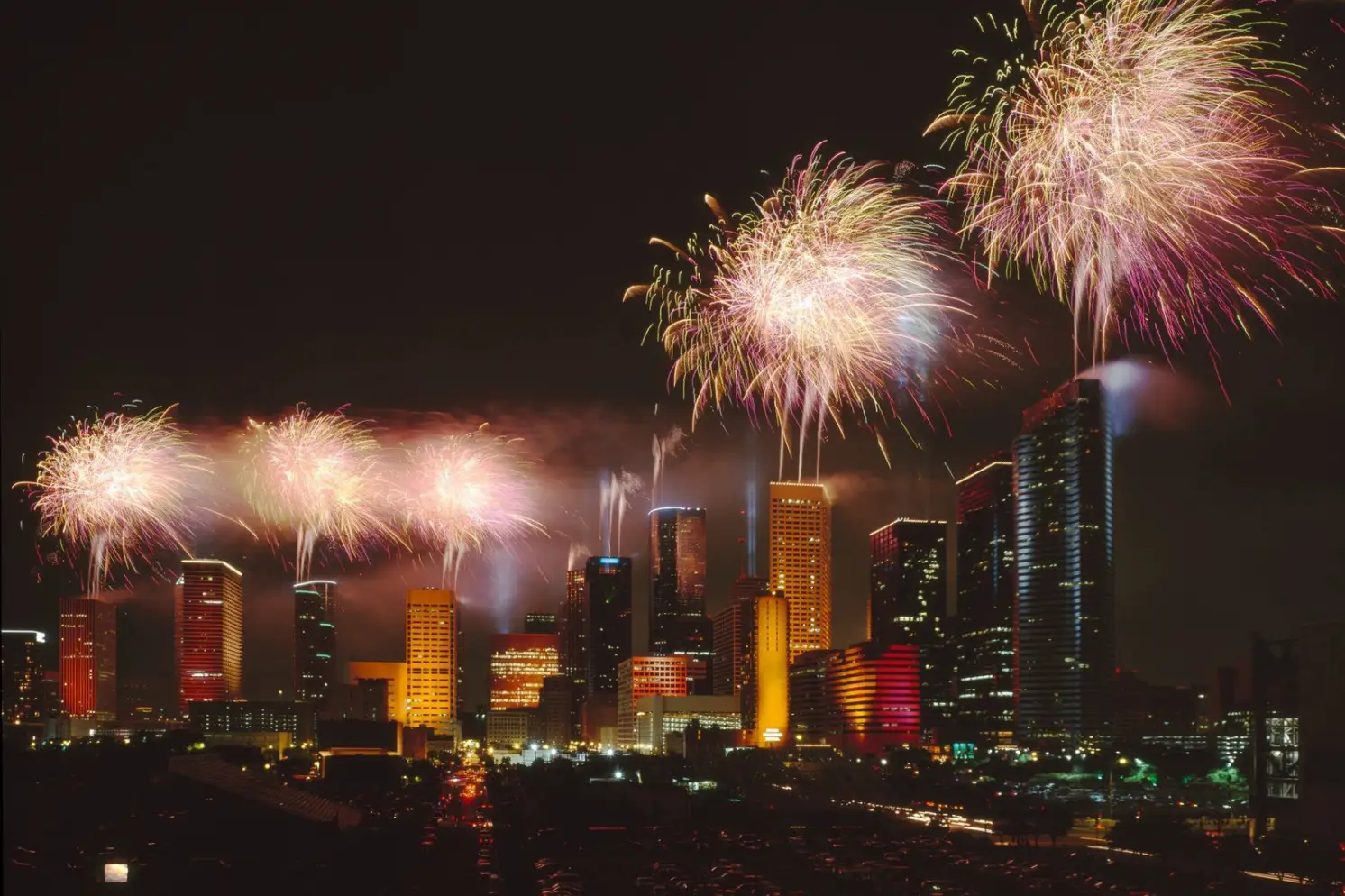 Colorful fireworks explode over the city skyline, illuminating skyscrapers at night, as festive celebrations fill the air—a perfect holiday spectacle for those relaxing at Rayford Crossing RV Resort.