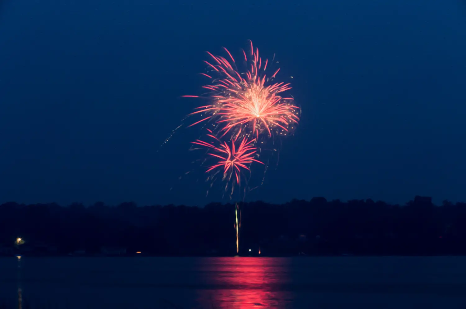 The fireworks display above Lake Conroe casts vibrant pink and red bursts, their colors dancing across the dark water, creating a dazzling spectacle perfect for the holidays.