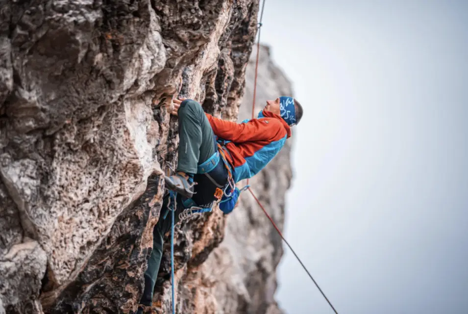 A climber in a blue and red outfit scales a steep rock face with ropes and gear, embodying the thrill of summer adventure ideas in Durango.