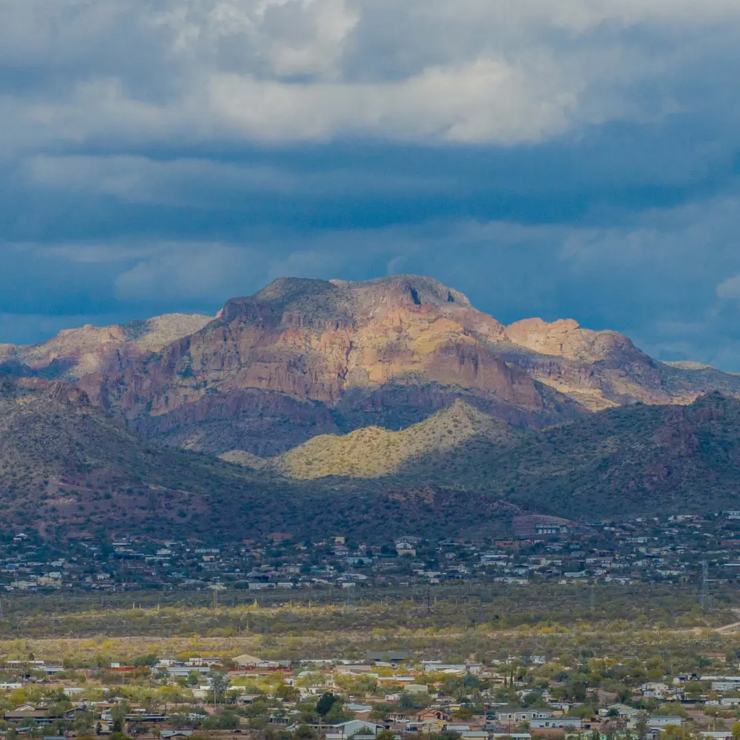 The view of the mountain range under a cloudy sky, with sunlight creating patches of light and shadow, is the perfect backdrop for Spring Adventures. In the foreground, the charming town of Apache Junction, AZ, nestles quietly amid nature’s grandeur.