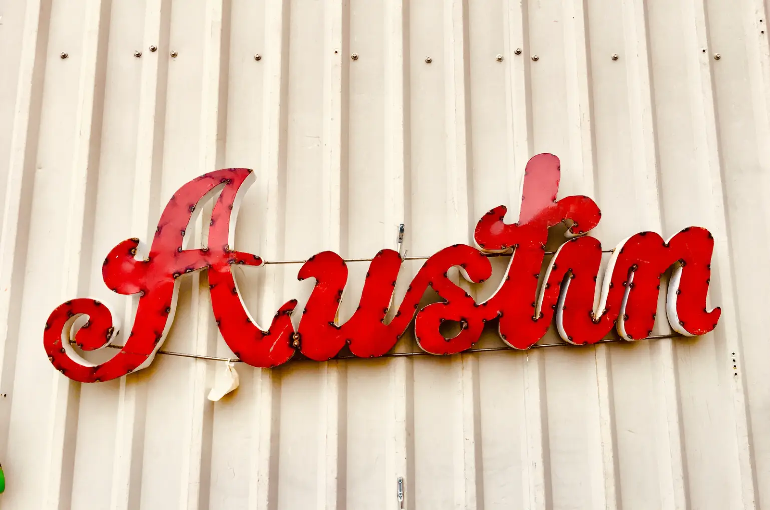 A vintage red metal sign spelling "Austin" hangs on a light corrugated wall, reminiscent of an auto draft's nostalgic charm.