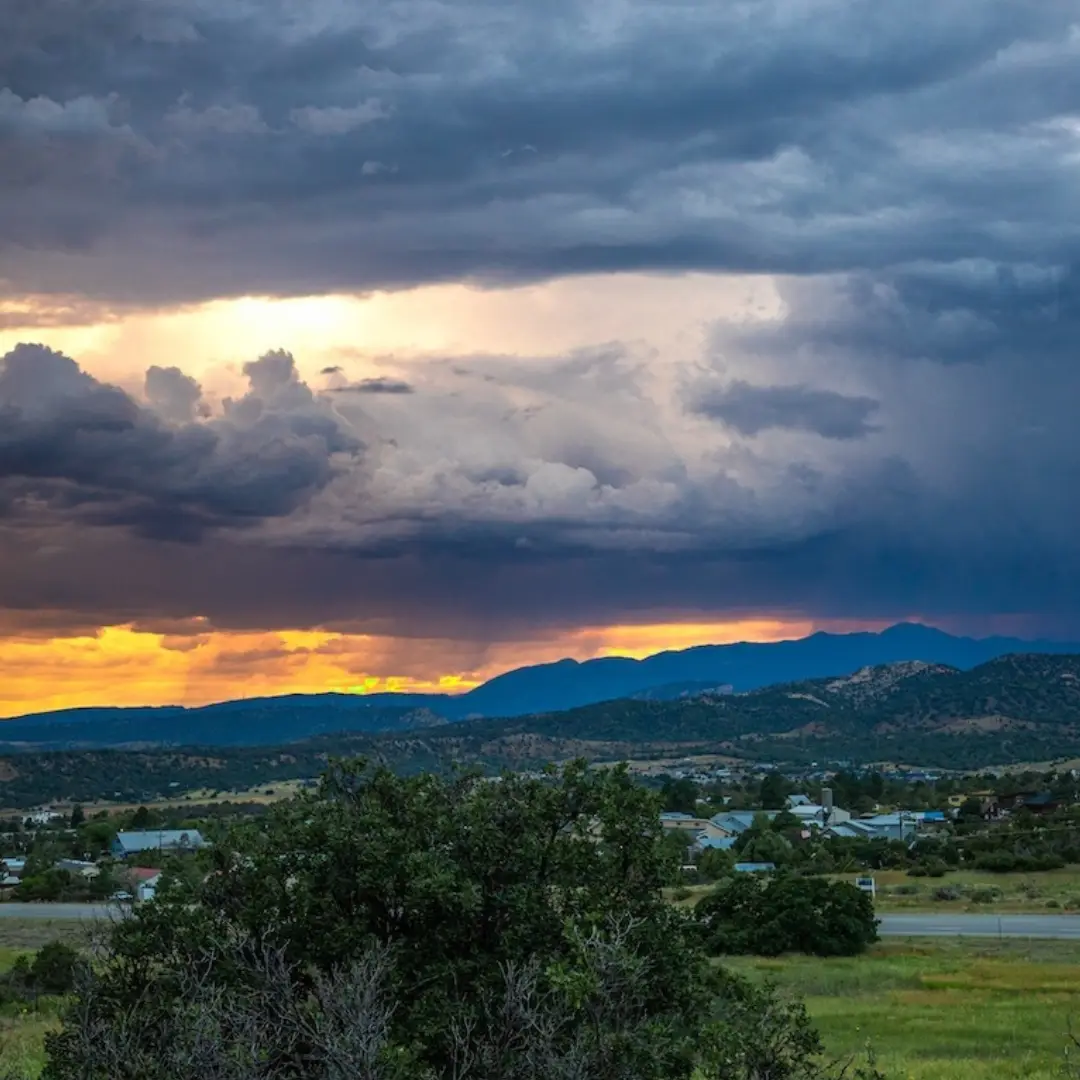 A dramatic sunset with dark storm clouds casts shadows over a rural landscape in Durango, Colorado. Hills and spring vegetation are visible in the foreground, setting the scene for an idyllic spring getaway.