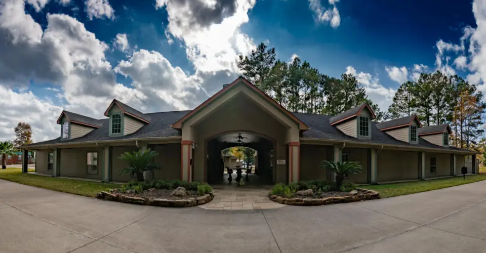 Nestled among the trees and under a cloudy sky, Rayford Crossing RV Resort features a large, single-story building with a convenient covered driveway.