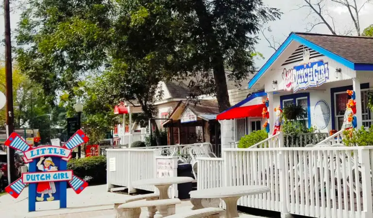 Exploring the street view of Little Dutch Girl store reveals patio seating, colorful signage, and decorative outdoor elements tucked under large trees, making it a charming attraction near Rayford Crossing RV Resort.