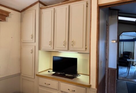 A small flat-screen TV sits on a counter built into a beige cabinet with upper and lower storage in a residential interior.