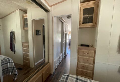 Bedroom with mirrored closet doors, built-in wooden drawers and cabinets, plaid bedding, and a hallway leading to another room.