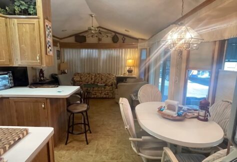 A cozy living area with a small kitchen on the left, a round dining table with chairs in the center, and a sofa with lamps against the far wall.