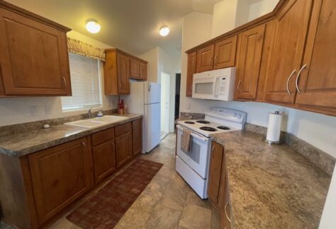 A kitchen with wooden cabinets, white appliances including a stove, microwave, and refrigerator, a double sink, and brown countertops.