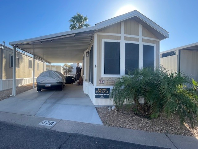 A small manufactured home with a covered driveway, two parked cars, a “Home For Sale” sign, and a palm tree in front. The home is marked with the number 476.