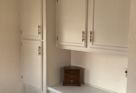 White built-in cabinets and drawers with brass handles are shown against a wall. A small wooden jewelry box sits on the surface beneath the upper cabinets.