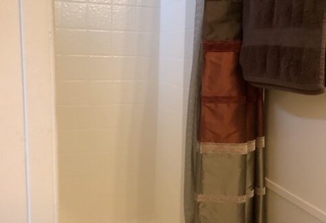 A small white tiled shower with a multicolored shower curtain partially open and a dark brown towel hanging on a rack nearby.