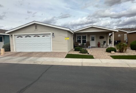 Single-story beige house with a white garage door, front porch with chairs, small garden, and a "Leasing" sign. Overcast sky in the background.