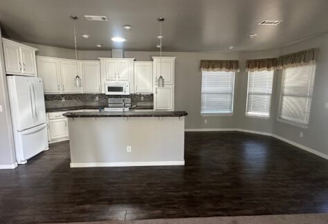 Modern kitchen with white cabinets, stainless steel appliances, dark countertops, and adjacent dining area with large windows and wood flooring.