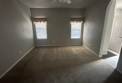 Empty room with beige carpet, two windows with blinds and valances, ceiling fan, and an arched doorway leading to another area.