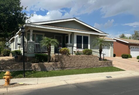 Single-story house with a covered front porch, palm trees, and a landscaped yard, situated on a corner lot with a driveway and attached garage.