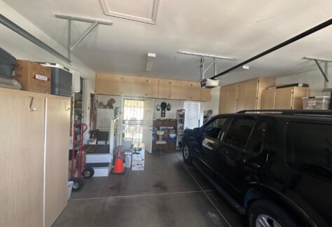 A black SUV is parked in a clean, organized garage with wooden cabinets, boxes, and various household items neatly stored along the walls.