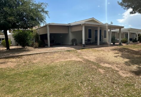 Single-story house with a covered porch, surrounded by a dry, patchy lawn and minimal landscaping, under a clear sky.